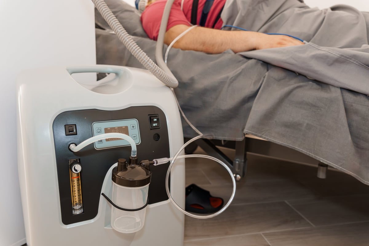 Equipamento de oxigenoterapia e concentrador de oxigênio ao lado do leito, representando o cuidado domiciliar de home care