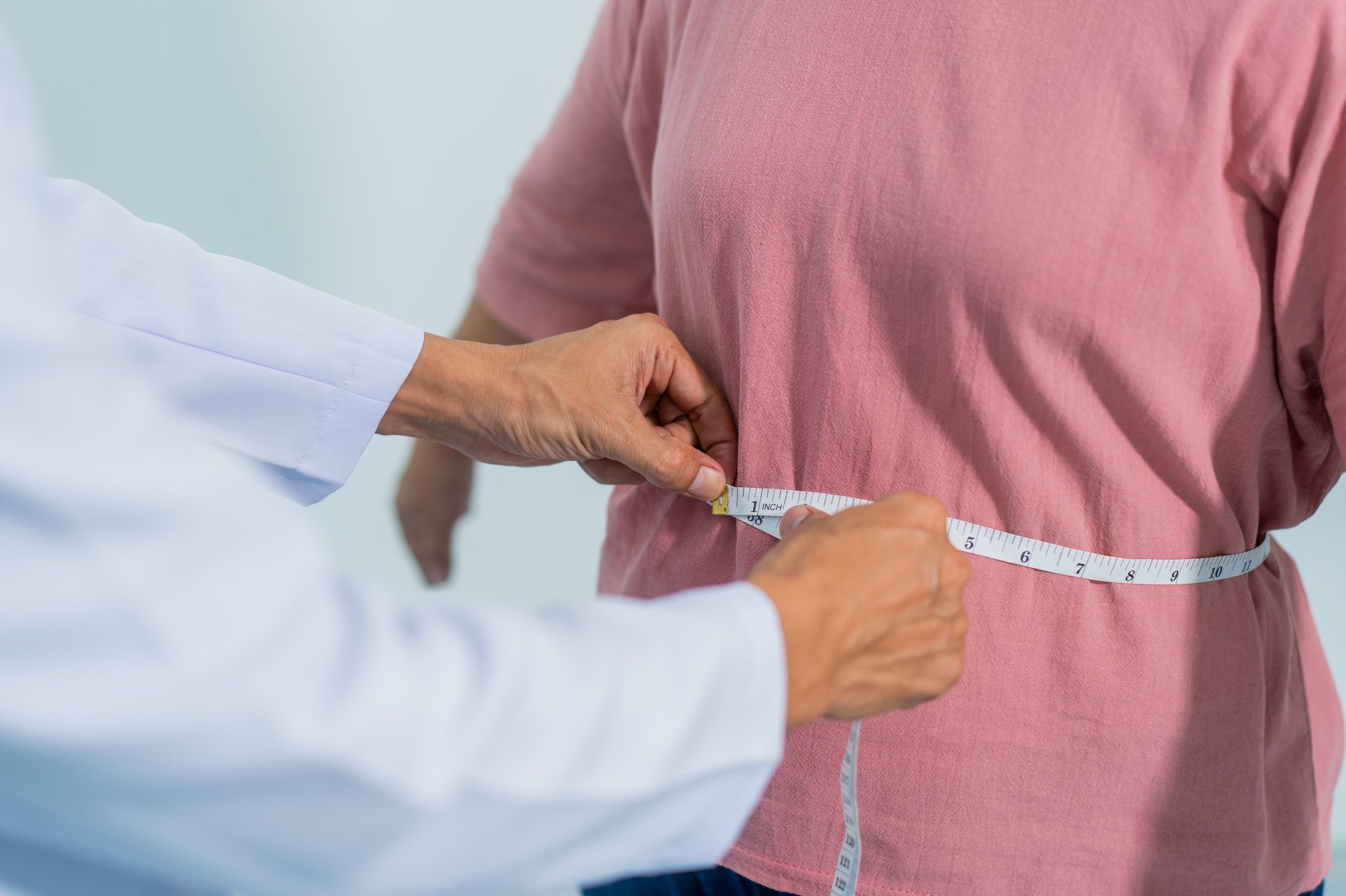 Profissional de saúde medindo a cintura de pessoa com sobrepeso, contexto de cuidado e tratamento de obesidade